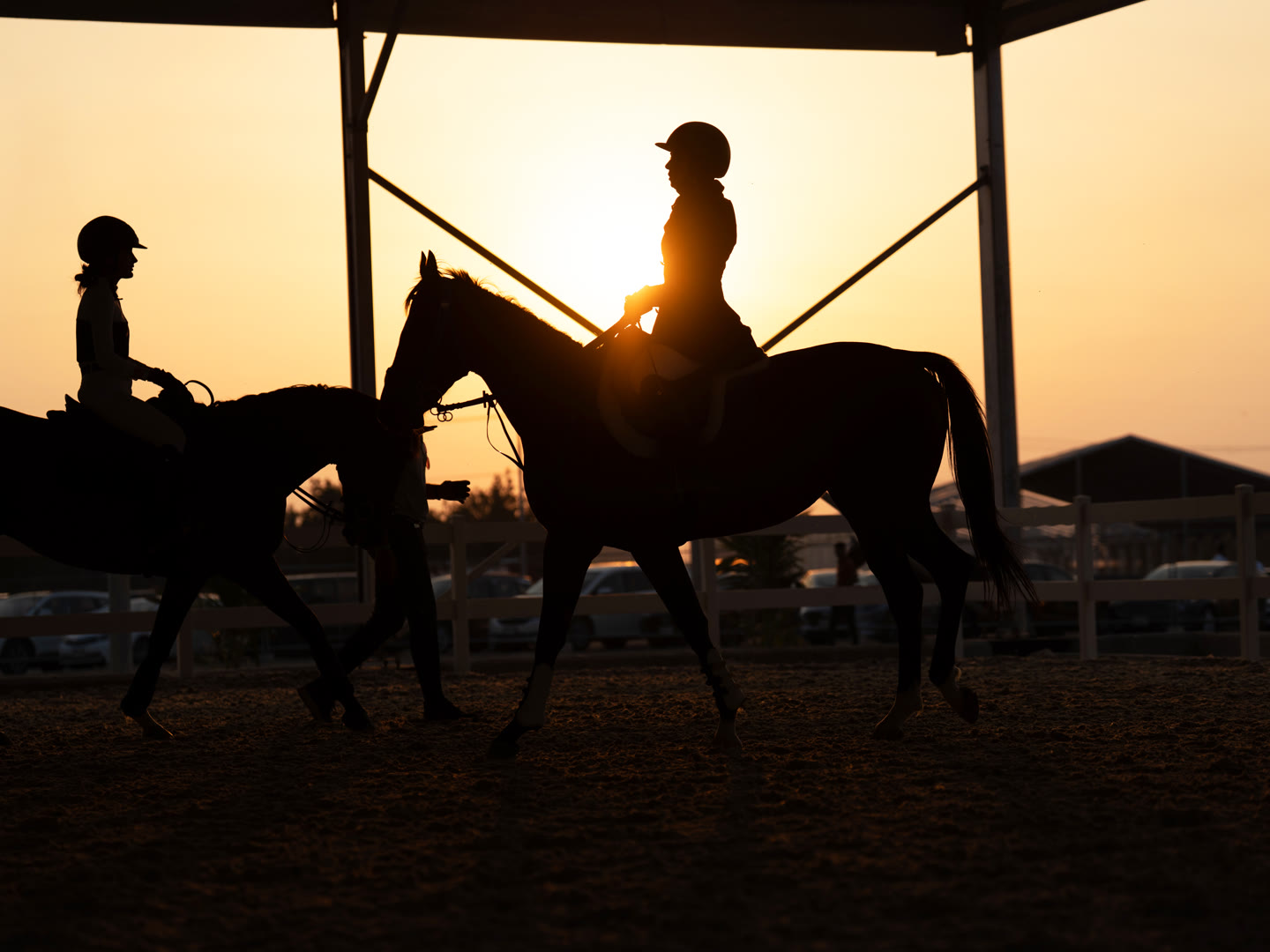 Two riders on horseback in silhouette against a golden sunset in the Trio Sporting arena